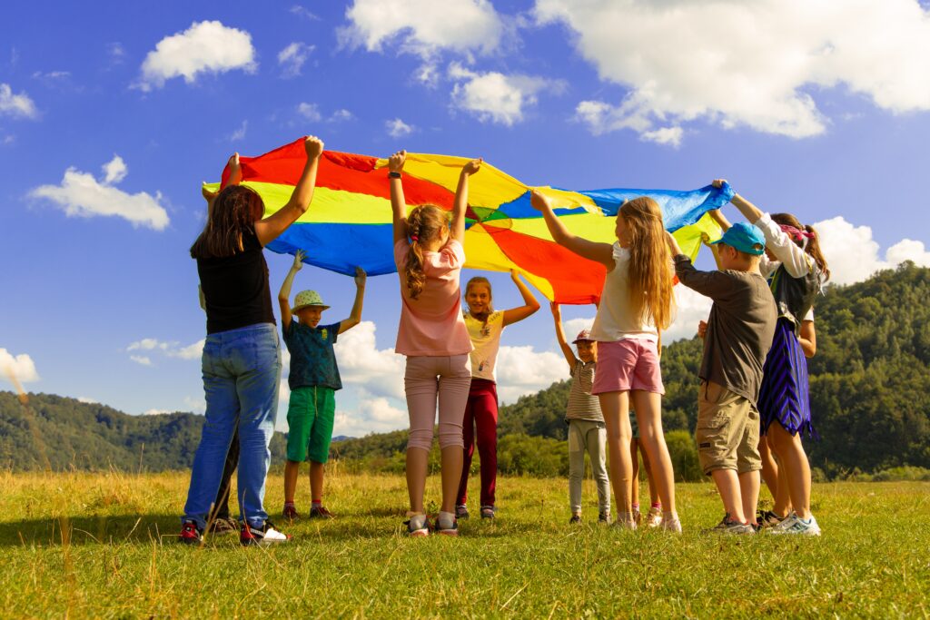 Children playing outside with a rainbow colored parachute.